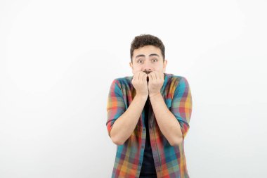 Parmaklarını ısıran damalı tişörtlü yakışıklı bir adam resmi. Yüksek kalite fotoğraf