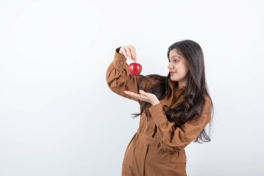 Beyaz duvarın üzerinde duran kırmızı elmalı esmer bir kız resmi. Yüksek kalite fotoğraf