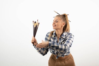 Beyaz bir duvarın üzerinde boya fırçaları tutan ve poz veren zevkli bir sanatçı. Yüksek kalite fotoğraf