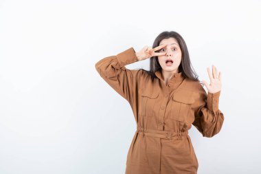 Beyaz duvara karşı zafer işareti gösteren esmer bir kadın modeli. Yüksek kalite fotoğraf