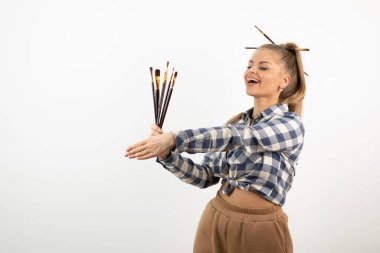 Beyaz bir duvarın üzerinde boya fırçaları tutan ve poz veren zevkli bir sanatçı. Yüksek kalite fotoğraf