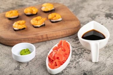 Tahta kesme tahtasına yerleştirilmiş taze, lezzetli suşi ruloları, karides ve zencefil dilimleri. Yüksek kalite fotoğraf