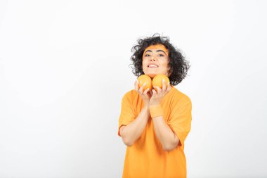 Turuncu tişörtlü kadın portakallarla poz veriyor.