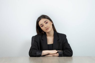 Esmer iş kadını işyerinde oturuyor ve kameraya bakıyor.