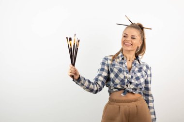 Beyaz bir duvarın üzerinde boya fırçaları tutan ve poz veren zevkli bir sanatçı. Yüksek kalite fotoğraf