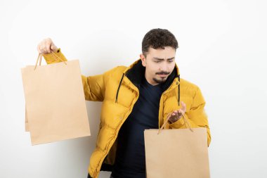 Beyaz bir duvarın üzerinde kağıt torbaları tutan genç bir adam. Yüksek kalite fotoğraf