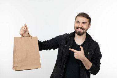 Beyaz bir duvarın üzerinden kağıt torbaları gösteren genç yakışıklı bir adam. Yüksek kalite fotoğraf