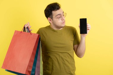 Elinde boş cep telefonu ve alışveriş torbaları olan yakışıklı bir adamın fotoğrafı. Yüksek kalite fotoğraf
