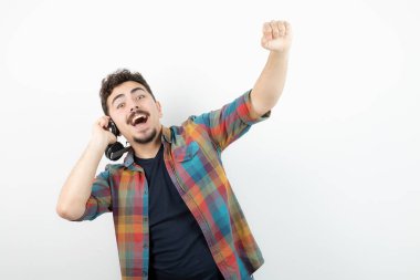 Beyaz bir duvarın üzerinde kulaklık tutan genç yakışıklı bir adam resmi. Yüksek kalite fotoğraf