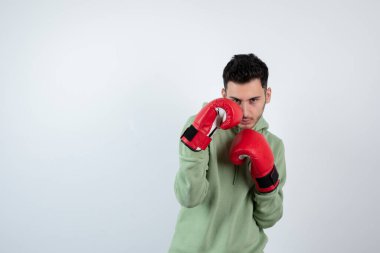 Kendine güvenen genç sporcu beyaz duvara karşı boks eldivenleriyle yumruk atıyor. Yüksek kalite fotoğraf