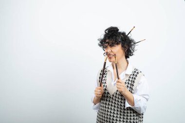 Beyaz bluzlu, boyalı fırçalar tutan kıvırcık esmer kadın. Yüksek kalite fotoğraf