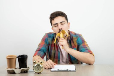 Genç adam çalar saatle masada oturuyor, fincanlar ve muz yiyor. Yüksek kalite fotoğraf