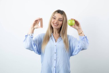 Gülümseyen mutlu bir kızın portresi. Beyaz duvarda yeşil elmalı çikolata tutuyor. Yüksek kalite fotoğraf