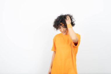 Turuncu tişörtlü kadın beyaz arka planda poz veriyor.