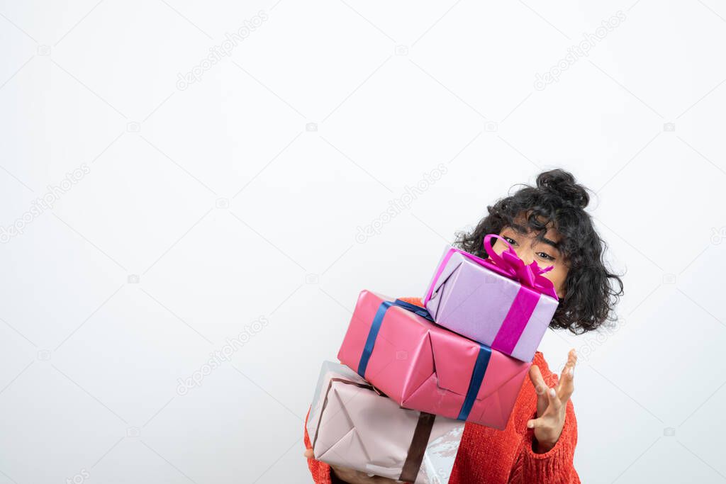 Image of short-haired curly girl in red sweater trying to hold gift boxes. High quality photo