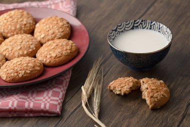 Tohumlu kırmızı yulaf ezmeli bisküvi ve ahşap zemin üzerinde bir kase taze süt. Yüksek kalite fotoğraf