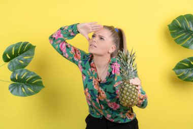 Taze ananaslı genç bir kadın sarı duvara poz veriyor. Yüksek kalite fotoğraf