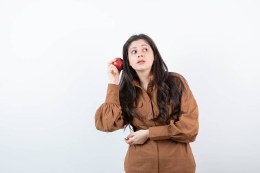 Beyaz duvarın üzerinde duran kırmızı elmalı esmer bir kız resmi. Yüksek kalite fotoğraf