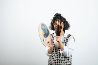 Kıvırcık saçlı genç bayan ressam palet tutuyor. Renkli ve fırçalı. Yüksek kalite fotoğraf