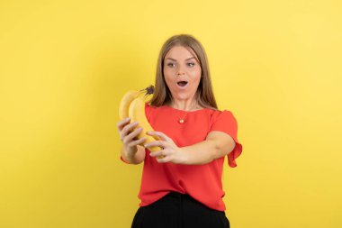 Sarı duvara karşı muzla poz veren komik, güzel bir genç kadın. Yüksek kalite fotoğraf