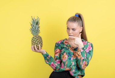 Sarı duvara karşı taze ananasları gösteren genç bir kadın. Yüksek kalite fotoğraf