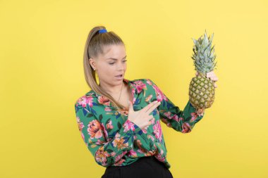 Sarı duvara karşı taze ananasları gösteren genç bir kadın. Yüksek kalite fotoğraf