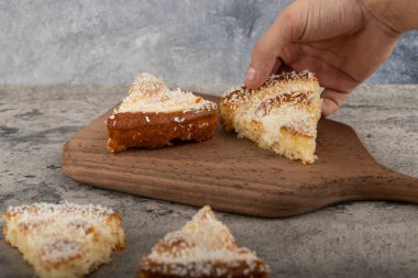 Erkek el, tahta kesme tahtasına yerleştirilmiş hindistan cevizi talaşı ile tatlı dilimini alıyor. Yüksek kalite fotoğraf