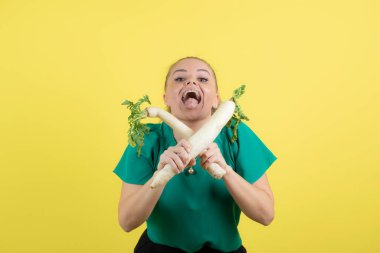 Sarı duvarda daikon turplarıyla poz veren güzel bir ev hanımı. Yüksek kalite fotoğraf