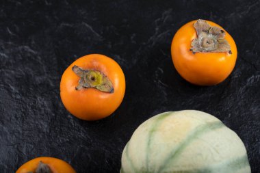 Siyah yüzeyde üç taze fuyu hurması ve kavun. Yüksek kalite fotoğraf