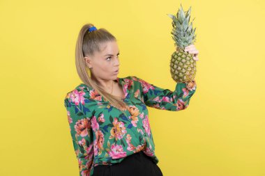 Taze ananaslı genç bir kadın sarı duvara poz veriyor. Yüksek kalite fotoğraf