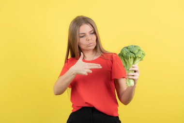 Sarı duvardaki brokoliyi gösteren güzel bir kadın modeli. Yüksek kalite fotoğraf
