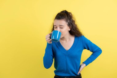 Sarı arka planda çay içen kıvırcık bir kız resmi. Yüksek kalite fotoğraf