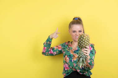 Sarı duvara karşı taze ananasları gösteren genç bir kadın. Yüksek kalite fotoğraf
