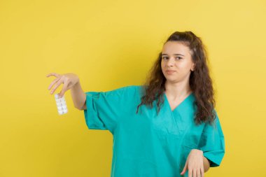 Üniformalı genç hemşire sarı duvarda tıbbi hapları gösteriyor. Yüksek kalite fotoğraf