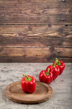 Wooden plate of ripe red bell peppers on stone surface. High quality photo