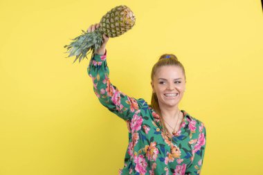 Taze ananaslı genç bir kadın sarı duvara poz veriyor. Yüksek kalite fotoğraf