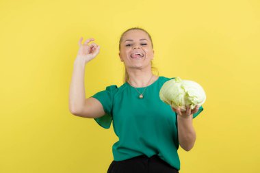 Sarı duvarın üzerinde yeşil lahanayla poz veren güzel bir kadının portresi. Yüksek kalite fotoğraf