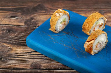 Tahta kesme tahtasına yerleştirilmiş taze, lezzetli suşi ruloları, karides ve zencefil dilimleri. Yüksek kalite fotoğraf