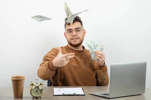 若いハンサムなビジネスマンは彼の机の上に座ってお金を投げる 高品質の写真 — ストック写真