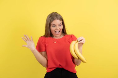 Sarı stüdyo arka planında muz tutan kendine güvenen genç bir kadın. - Evet. Yüksek kalite fotoğraf
