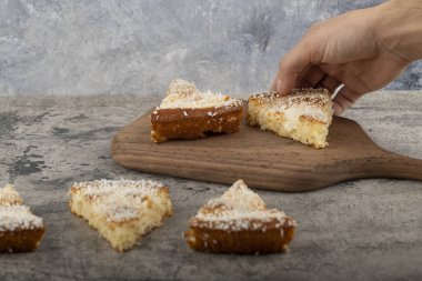 Erkek el, tahta kesme tahtasına yerleştirilmiş hindistan cevizi talaşı ile tatlı dilimini alıyor. Yüksek kalite fotoğraf