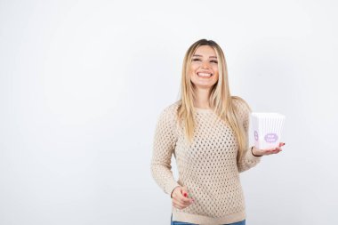 Beyaz duvara karşı duran ve elinde patlamış mısır taşıyan genç bir kadın resmi. Yüksek kalite fotoğraf