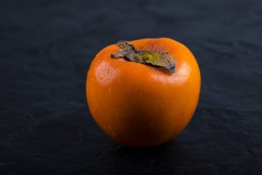 Siyah yüzeye yerleştirilmiş tek bir taze fuyu hurması. Yüksek kalite fotoğraf