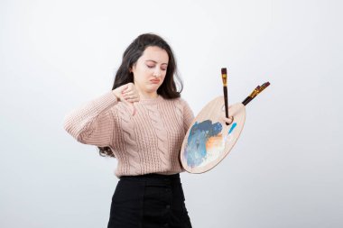 Renkli paletli kadın ressam ve baş parmağını aşağı gösteren boya fırçaları. Yüksek kalite fotoğraf