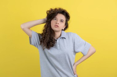 Sarı arka planda genç bir kızın saçına dokunurken kameraya baktığı fotoğraf. Yüksek kalite fotoğraf