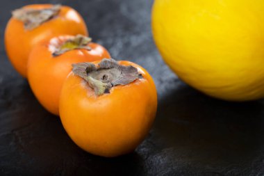 Siyah yüzeyde üç taze fuyu hurması ve sarı kavun. Yüksek kalite fotoğraf