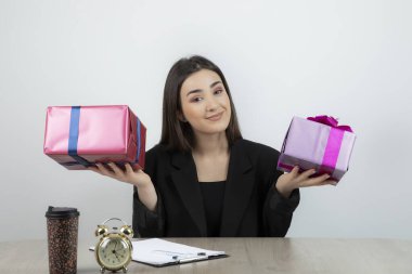 İş yerinde elinde hediyelerle oturan iş kadınının portresi.