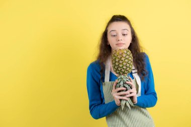 Sarı duvarda olgun ananaslı önlüklü genç kızın fotoğrafı. Yüksek kalite fotoğraf