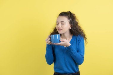Sarı arka planda çayına bakan kıvırcık bir kız resmi. Yüksek kalite fotoğraf