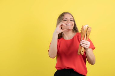 Sarı duvara karşı spatula ve kepçe tutan genç bir kadının portresi. Yüksek kalite fotoğraf